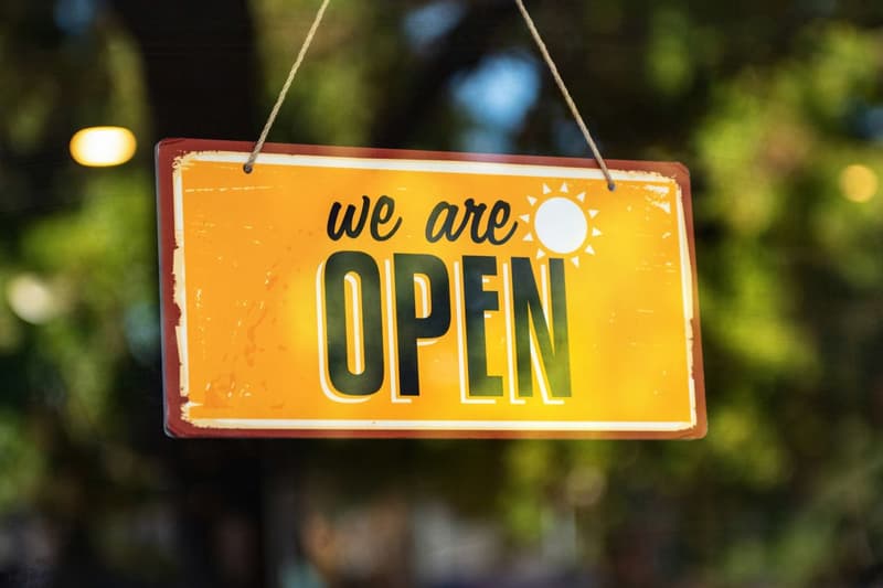 Warm amber 'we are open' shop sign against green foliage